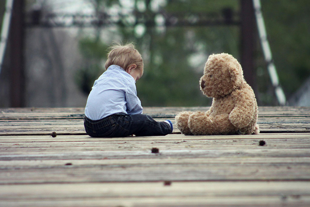 Kind sitzt neben Teddybär im Freien